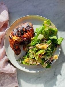 a chicken quarter on a plate with salad