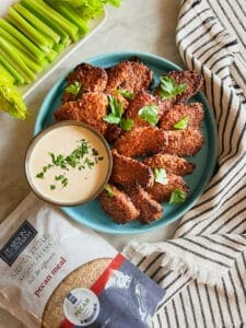 Gluten free pecan crusted chicken tenders on a blue plate with a peach dipping sauce, celery and a striped napkin