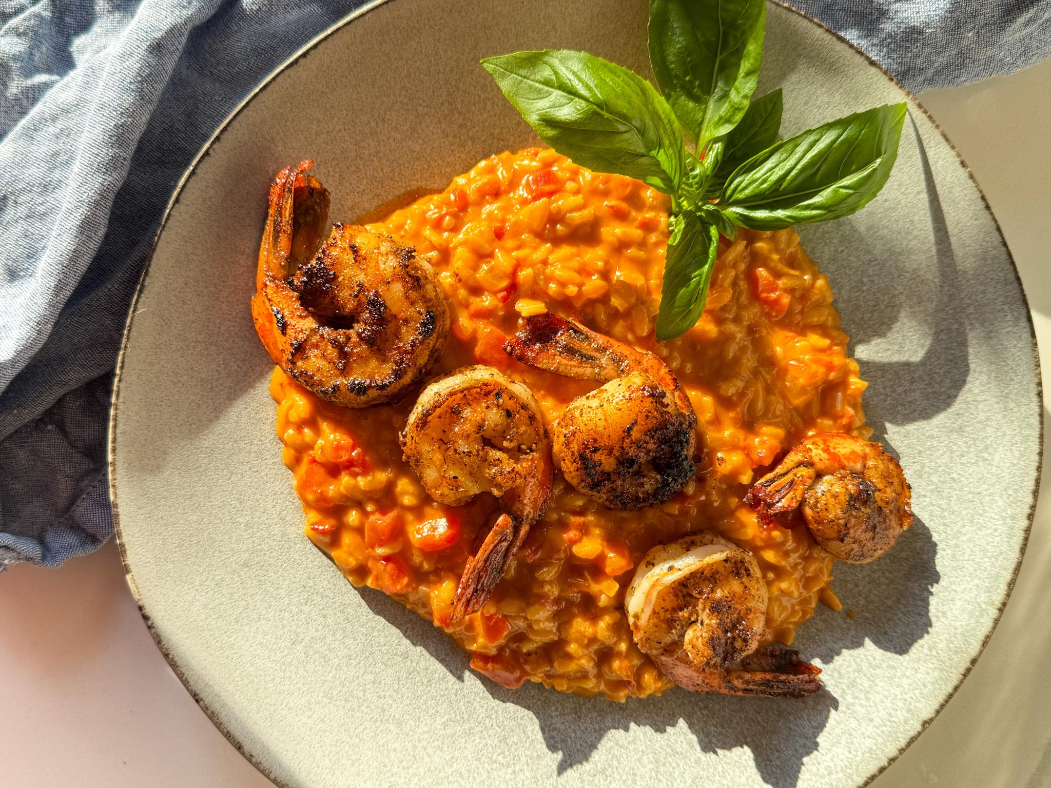 Tomato risotto on a plate with basil and seared shrimp.