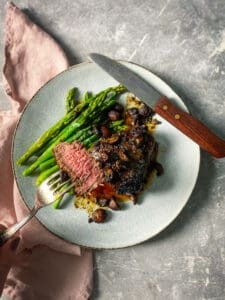 Medium rare steak piece on a fork with a plate with mushrooms and asparagus