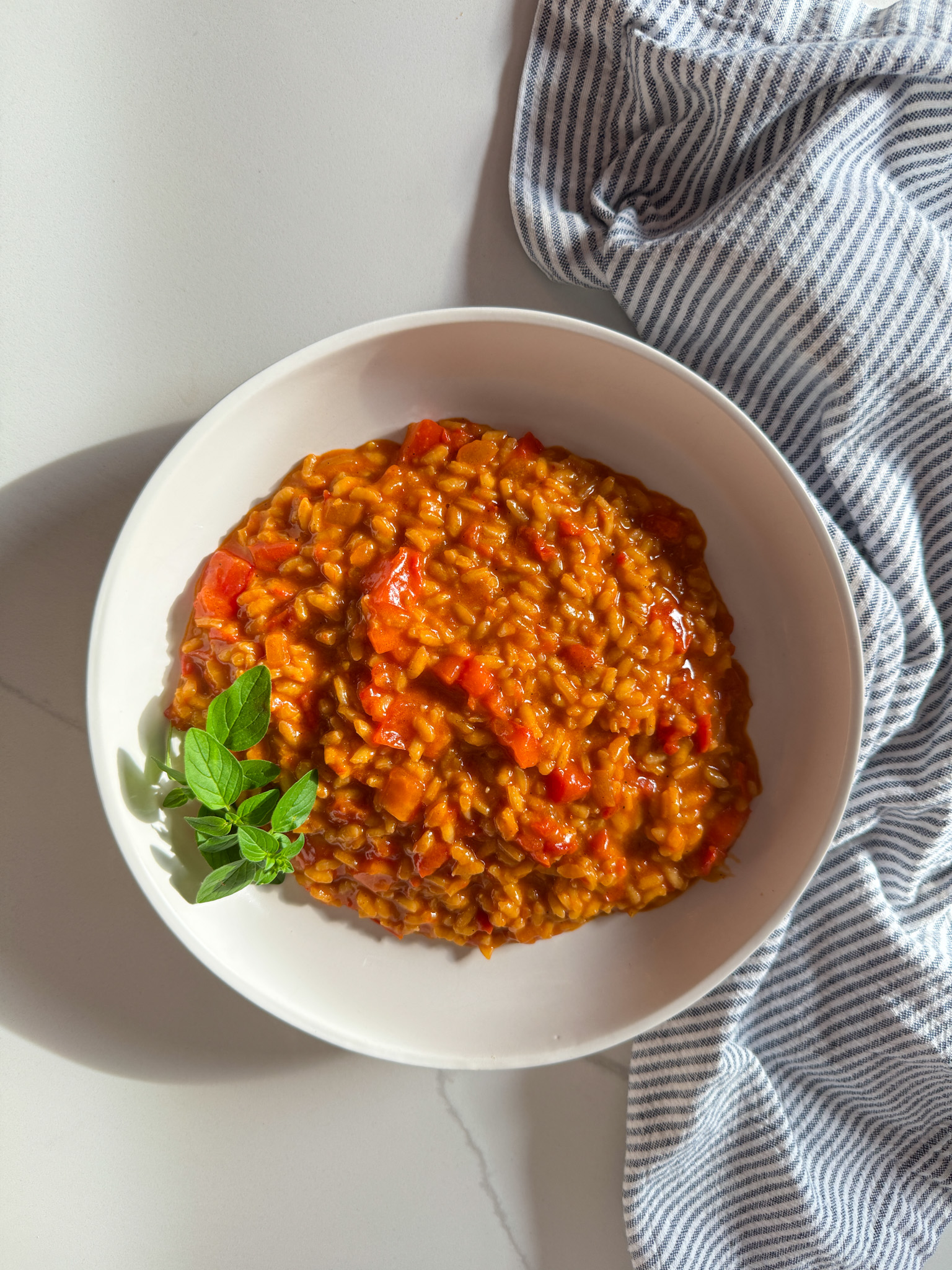 bowl of tomato risotto with parsley and a stripe napkin