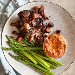 steak and mushrooms and asparagus and cheese popover on a plate with a blue napkin