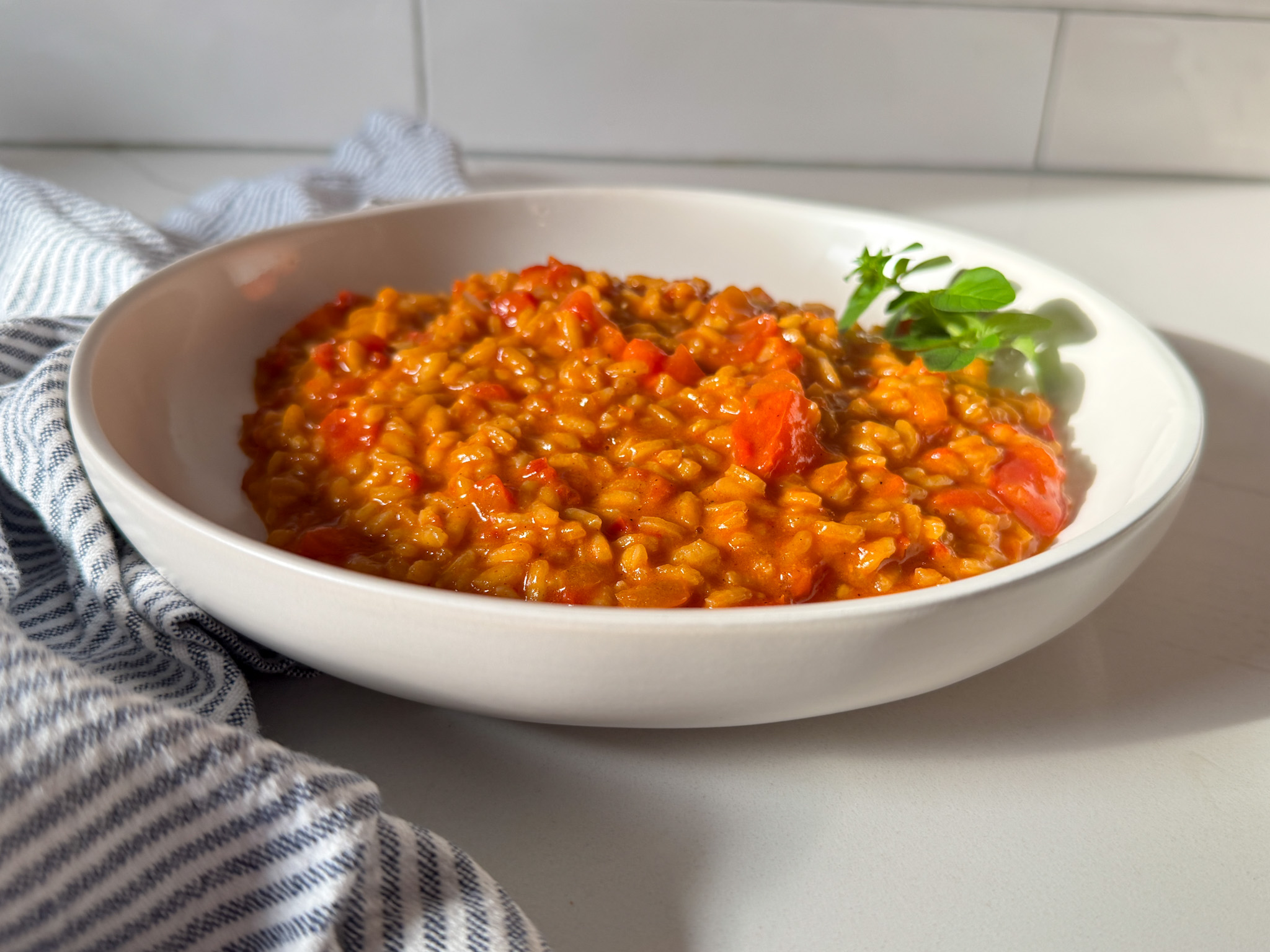 horizontal image of tomato risotto in a white bowl with a stripe napking and parsley