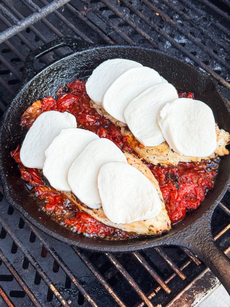 mozzarella topped chicken in a pan with tomatoes on a grill
