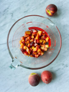 peaches cut up in a bowl with whole peaches sitting beside bowl