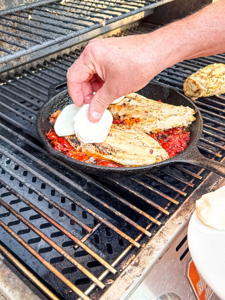 hand putting mozzarella on caprese chicken on the gril
