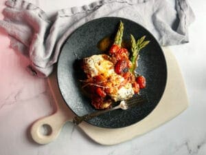 caprese grilled chicken on asparagus on a black plate on a cutting board with a napkin