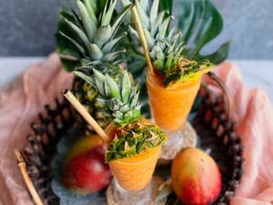 2 mango daiquiris with a pineapple and 2 mangos on a tray