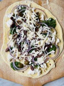 Greek pizza uncooked on a wooden pizza peal