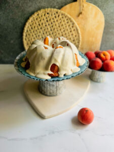 peach cobbler pound cake on a stand with a bowl of peaches