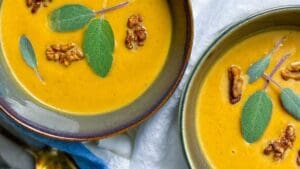 horizontal image of 2 bowls of butternut squash soup with sage leaves and walnuts