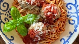 horizontal shot up close of a blowl with spaghetti and meatballs and basil