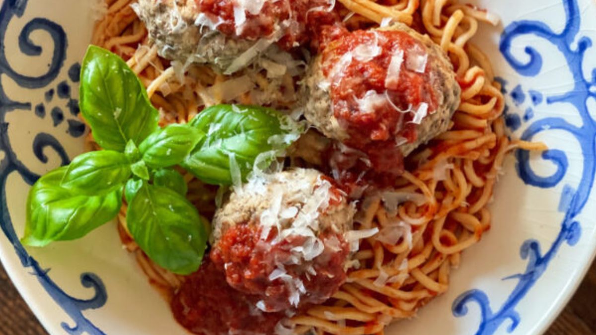 horizontal shot up close of a blowl with spaghetti and meatballs and basil