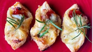 3 baked brie bites on a red plate with rosemary