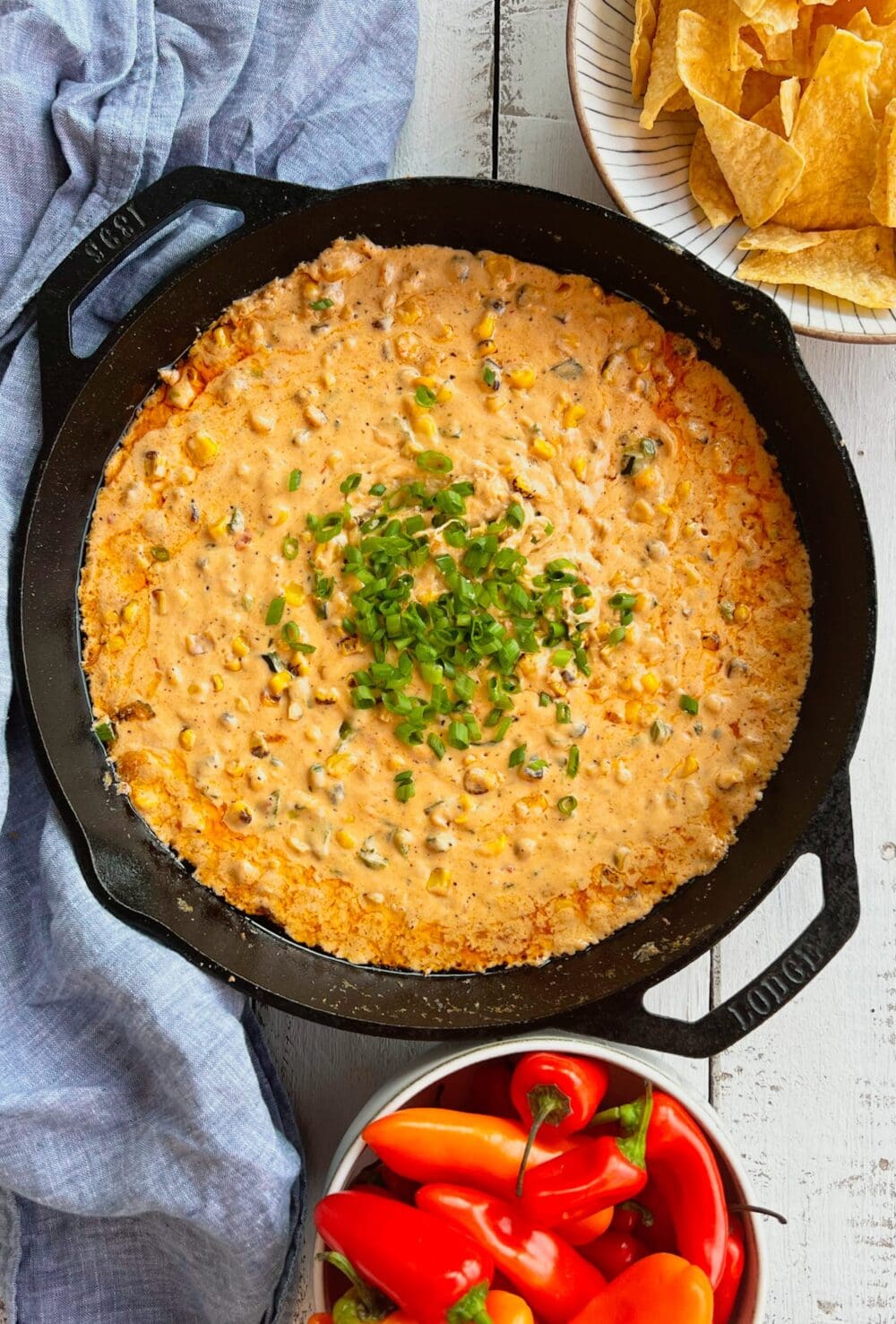 Smoked poblano and corn cream cheese dip in a cast iron pan with chips and peppers and a blue napkin