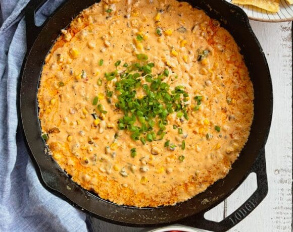 Smoked poblano and corn cream cheese dip in a cast iron pan with chips and peppers and a blue napkin