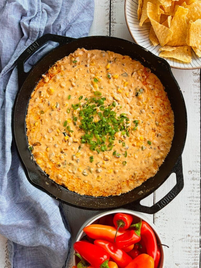 Smoked poblano and corn cream cheese dip in a cast iron pan with chips and peppers and a blue napkin
