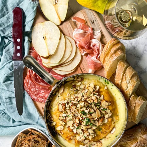 baked brie with fig jam and pears and toasted almonds on a board with meats and bread and crackers