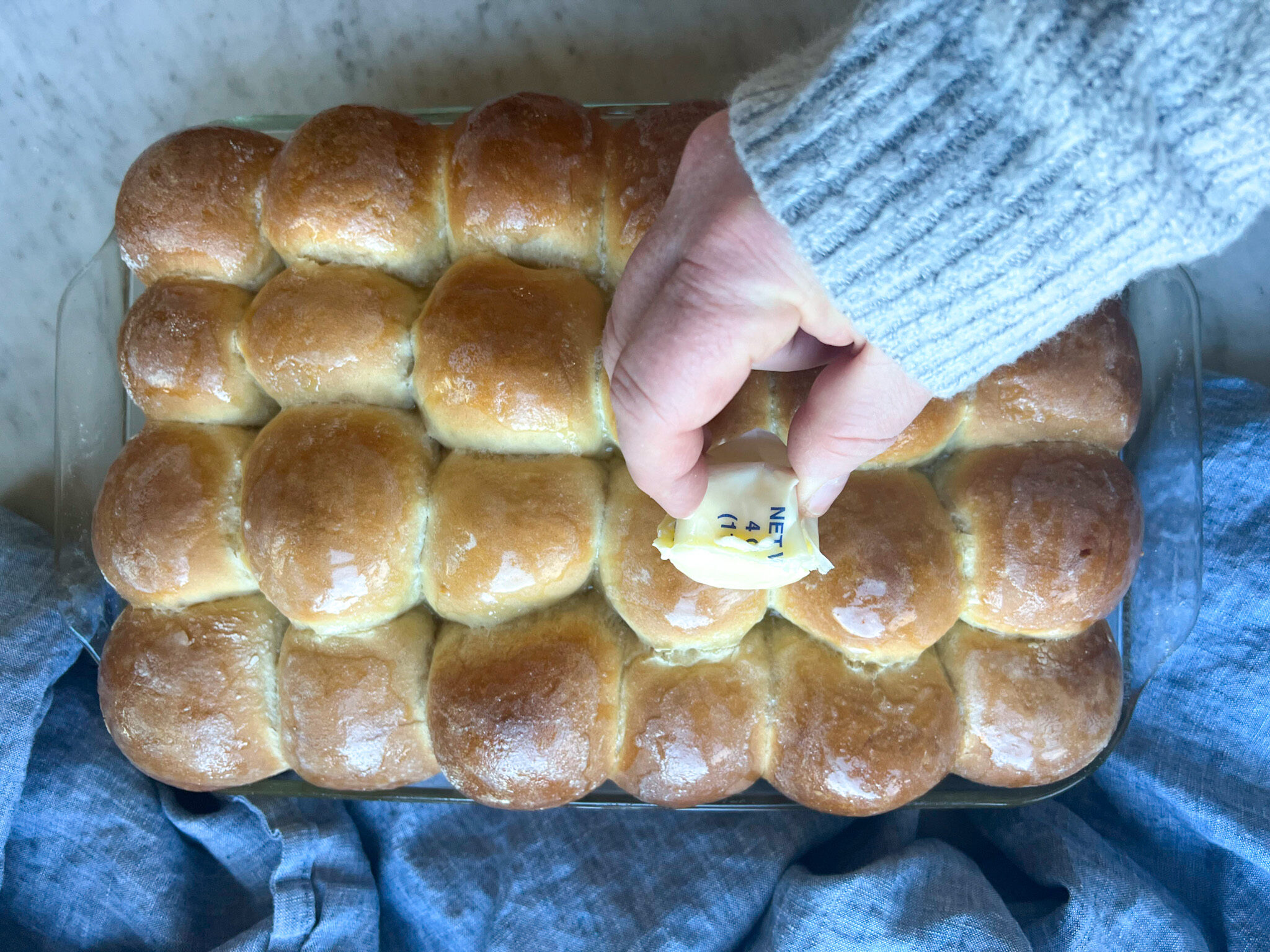 yeast rolls with a hand rubbing butter over the top