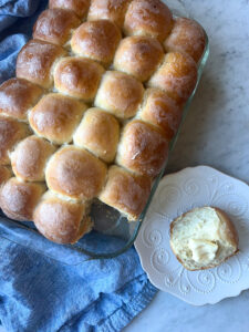 yeast rolls in a pan with one roll on a plate and a blue napkin