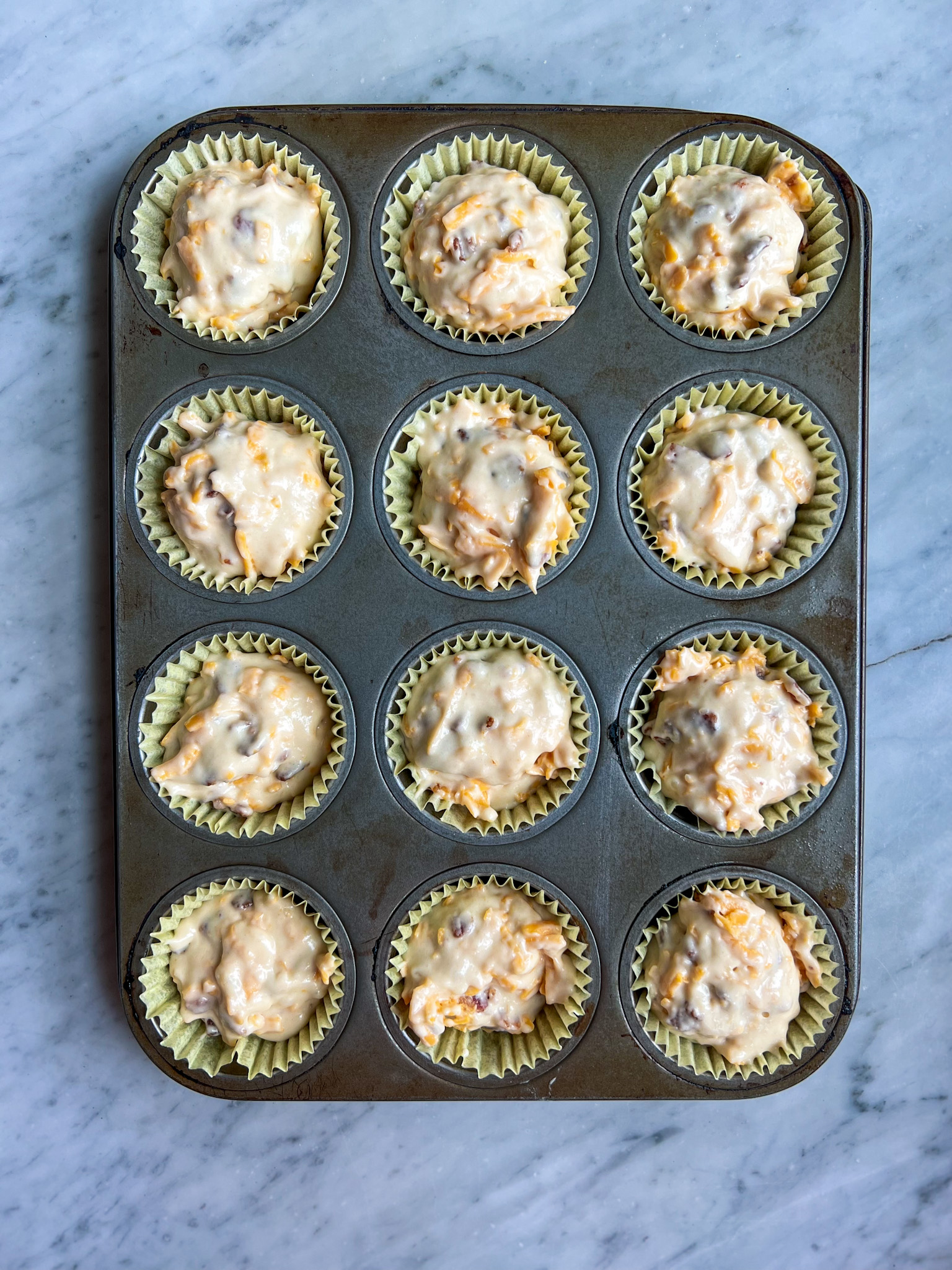 bacon cheese muffin batter in a muffin tin waiting to be baked