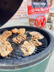 smoked grilled chicken thighs on the grill with western bbq cherry wood chunks in the background