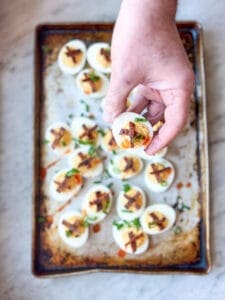 Smoked Deviled Eggs with Smoked Bacon Candy and Green onions and a hand holding one of the eggs