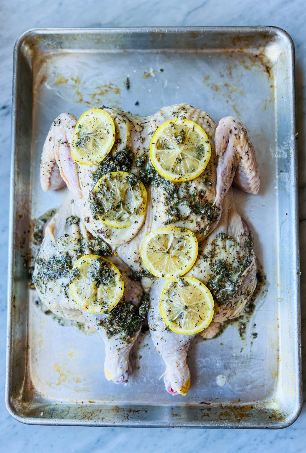 Greek seasoning and lemons on a spatchcocked chicken on a sheet pan