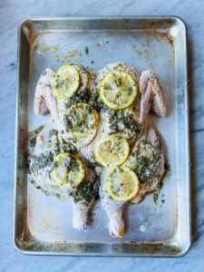 Greek seasoning and lemons on a spatchcocked chicken on a sheet pan