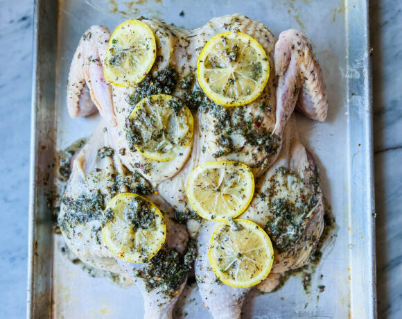 Greek seasoning and lemons on a spatchcocked chicken on a sheet pan