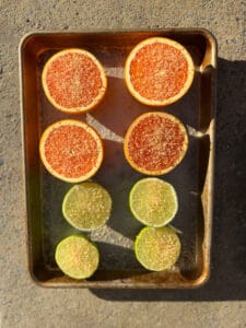 cara cara oranges and limes cut in half and sprinkled with turbinado sugar on a sheet pan