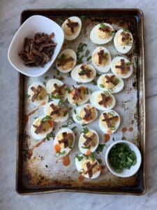 smoked deviled eggs and bacon and green onions on a tray
