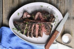 T bone steak cut and on a plate with a knife and a blue napkin