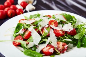 arugula and cherry tomato saad with shaved parmesan cheese on a white plate