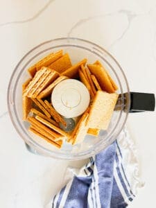 broken up graham crackers in a food processor and a blue and white towel