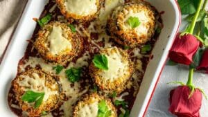 eggplant parmesan stacks in a pan with red roses on the side