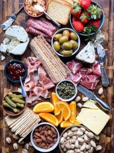 Charcuterie board with oranges, strawberries, crackers, pickles, nuts, meats and cheeses