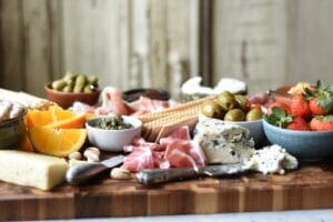 Charcuterie board with oranges, strawberries, crackers, pickles, nuts, meats and cheeses