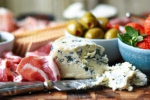 Bleu Cheese with knife and prosciuotto and crackers and olives in a bowl