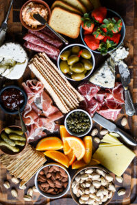 Charcuterie board with oranges, strawberries, crackers, pickles, nuts, meats and cheeses