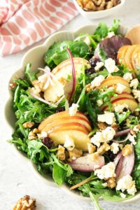 Apple walnut salad in a bowl with a bowl of walnuts and a napkin