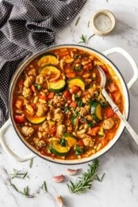 Sausage casserole in a white pan with handles and a spoon and napkin