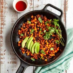 chorizo and sweet potato hash in a cast iron skillet with avocados and a napkin