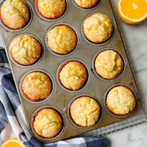 orange poppyseed muffins in a pan with a navy and white napkin and a half orange