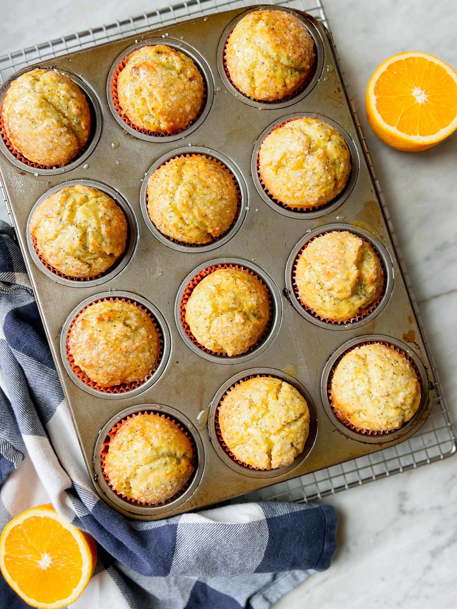 orange poppyseed muffins in a pan with a navy and white napkin and a half orange