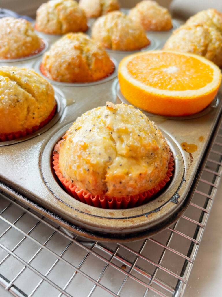 orange poppyseed muffins in a pan with a half an orange