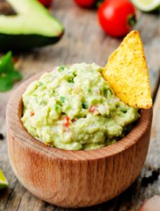 mango guacamole in a wooden bowl with a chip