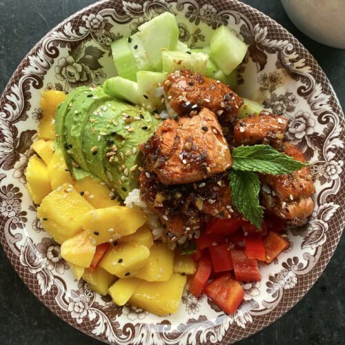 brown and white latice bowl with cucumber, salmon, red pepper, mango, pineapple, avocado and mint over rice