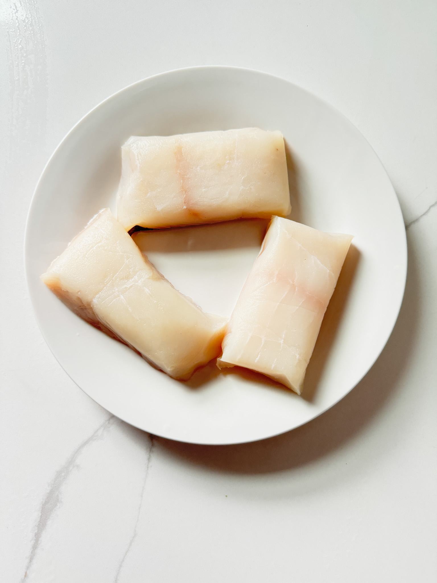 3 pieces of halibut on a white plate, uncooked