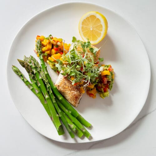 pan seared halibut with mango salsa, a lemon and asparagus on a plate